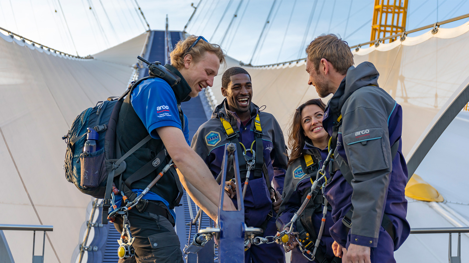 A group of 4 climbers stood on top of the O2 arena wearing climbing harnesses