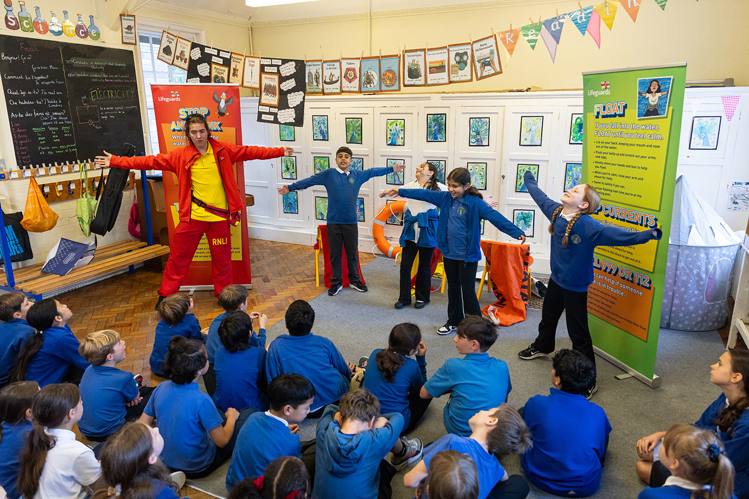 A lifeguard stood giving a water safety demonstration to a group of school children.